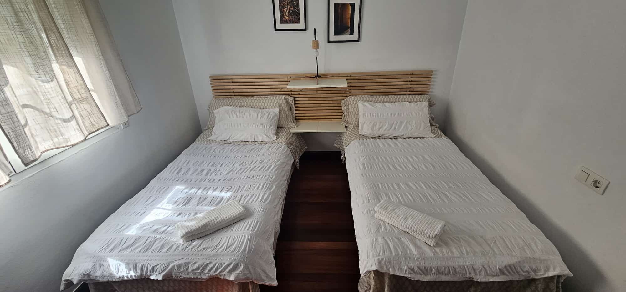 A twin room with two single beds, a wooden headboard, a bedside table, and a window with curtains.