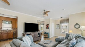 Una sala de estar amplia con un televisor de pantalla plana grande, un ventilador de techo y un comedor con mesa y sillas de madera.