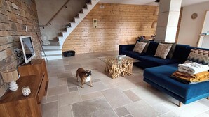 Een woonkamer met een blauwe bank, een houten salontafel, een hond, een trap en een stenen muur.