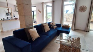 Een moderne woonkamer met een blauwe modulaire bank, een glazen salontafel en een stenen zuil.