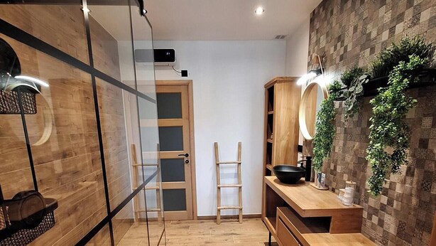 Een moderne badkamer met houten vloer, een glazen douchecabine, een houten wastafelmeubel met spiegel en een wandplant.