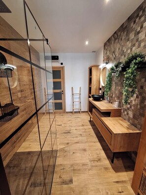 A modern bathroom with wooden flooring, a glass shower enclosure, a wooden vanity with a mirror, and a wall-mounted plant. - Completely renovated house in the heart of Provence (Bésignan)