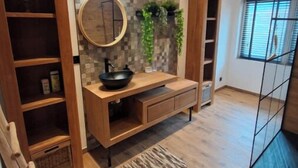 Een moderne badkamer met een houten wastafelmeubel, een ronde spiegel en een betegelde achterwand.