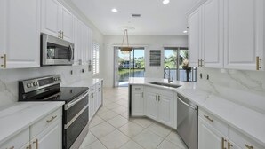 A modern kitchen with white cabinetry, stainless steel appliances, and a view to the outside.