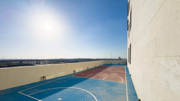 Una cancha de baloncesto al aire libre con vista despejada del entorno, incluyendo un puente y edificios a lo lejos.