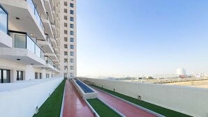 Un edificio moderno con un largo y estrecho sendero bordeado por césped artificial verde y pavimento rojo, que conduce a una entrada con portón.