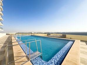 A rooftop swimming pool with clear blue water, a tiled edge, and a view of the cityscape in the background. - Free Housekeeping Visits During Your Stay - Stayshort - Comfortable 1 Bed in Jebel Ali Sleeps 2 With Balcony (Dubai)