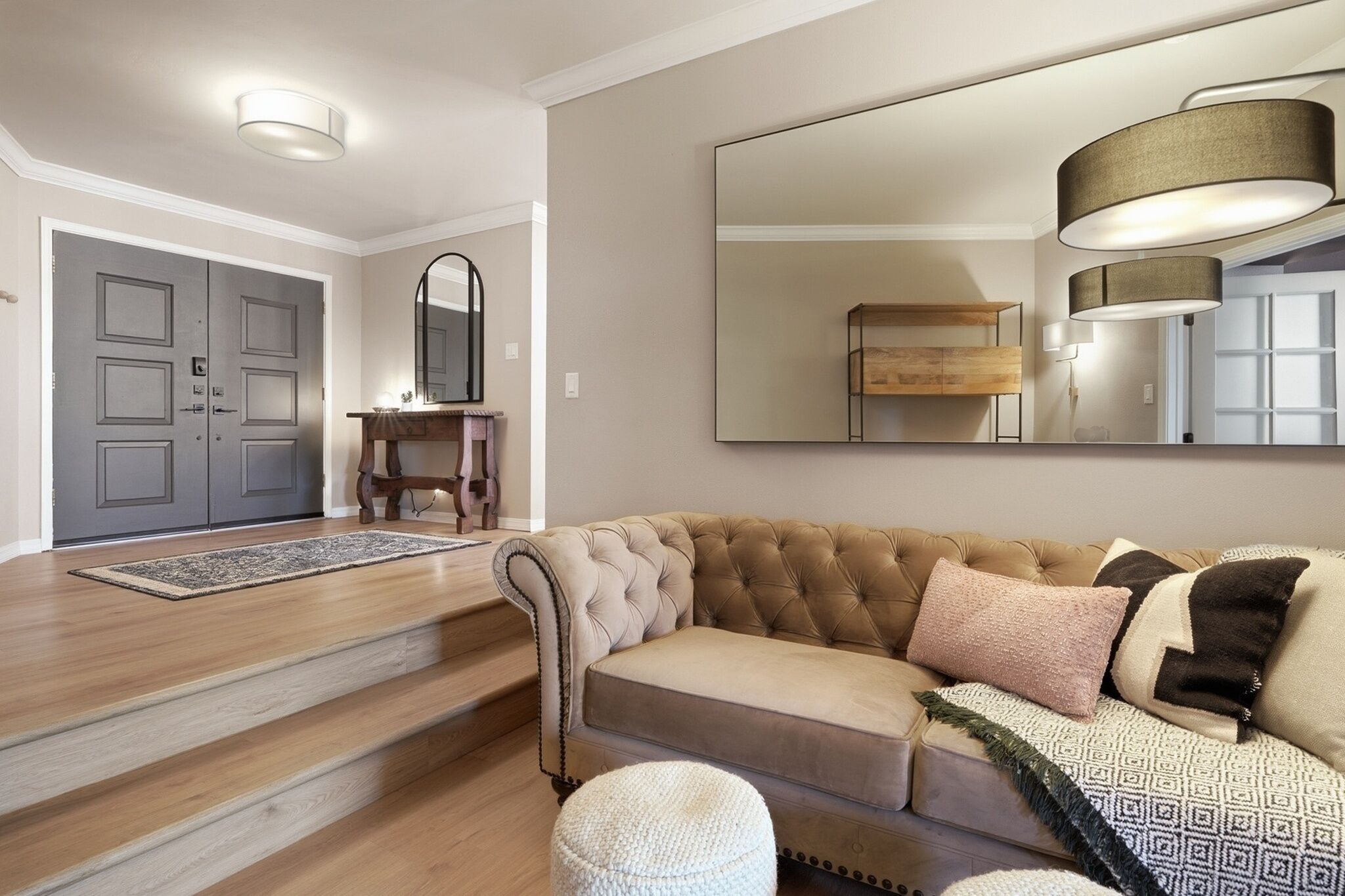 Una sala de estar con un sofá color beige, un espejo y una mesa de centro de madera.