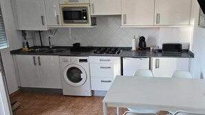 Una cocina compacta equipada con lavadora, microondas, tostadora y una pequeña mesa.