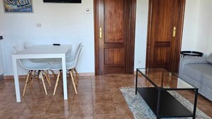Una sala de estar con un sofá, una mesa de comedor con sillas, una mesa de centro y una zona de cocina con mostrador y armarios.