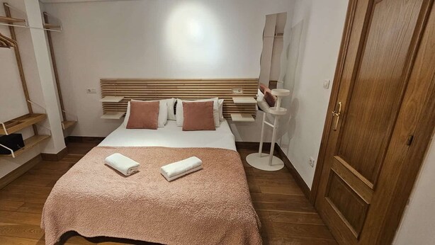 Un dormitorio con cama, cabecera de madera, mesitas de noche, un armario y un radiador.
