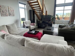 A modern living room with a sofa, armchairs, a coffee table, a TV, and a staircase. - Qu'Appelle Valley Getaway – Hot Tub with Beautiful Views, Sleeps 10 (Fairy Hill)