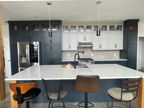 A modern kitchen with a central island, dark cabinets, stainless steel appliances, and bar stools.