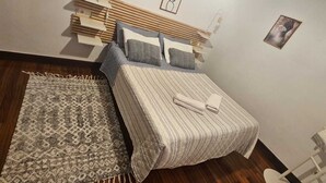 A neatly made bed with a striped bedspread and pillows, a patterned rug, and a wooden headboard. - Bizkar Bare Apartamento 4 (Sopuerta)