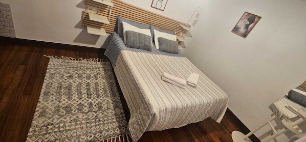 A neatly made bed with a striped bedspread and pillows, a patterned rug, and a wooden headboard.