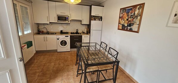 A compact kitchen with a washing machine, microwave, and dining table with chairs. - Bizkar Bare Apartamento 4 (Sopuerta)