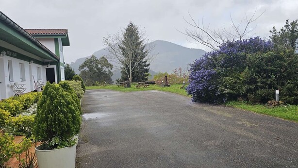 A building with a green roof, a paved driveway, and a mountain in the background. - Bizkar Bare Apartamento 4 (Sopuerta)