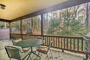 Un espace extérieur abrité, équipé d’une table et de chaises, d’un barbecue et offrant une vue sur une forêt.