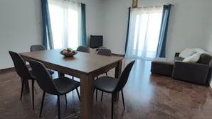 Ein Zimmer mit Esstisch, Stühlen, einer Couch und einem Fernseher.