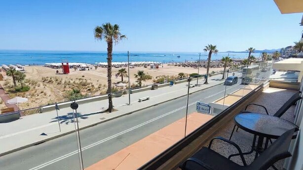 Ein Balkon mit Blick auf einen Strand, eine Straße und ein rotes Gebäude.