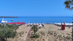 Ein Strand mit Liegestühlen und Sonnenschirmen, einem Weg und einer entfernten Küstenlinie.
