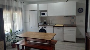 A compact kitchen with white cabinets, a microwave, a sink, and a wooden table. - El Rincon de San Fermin (Zizur Mayor)