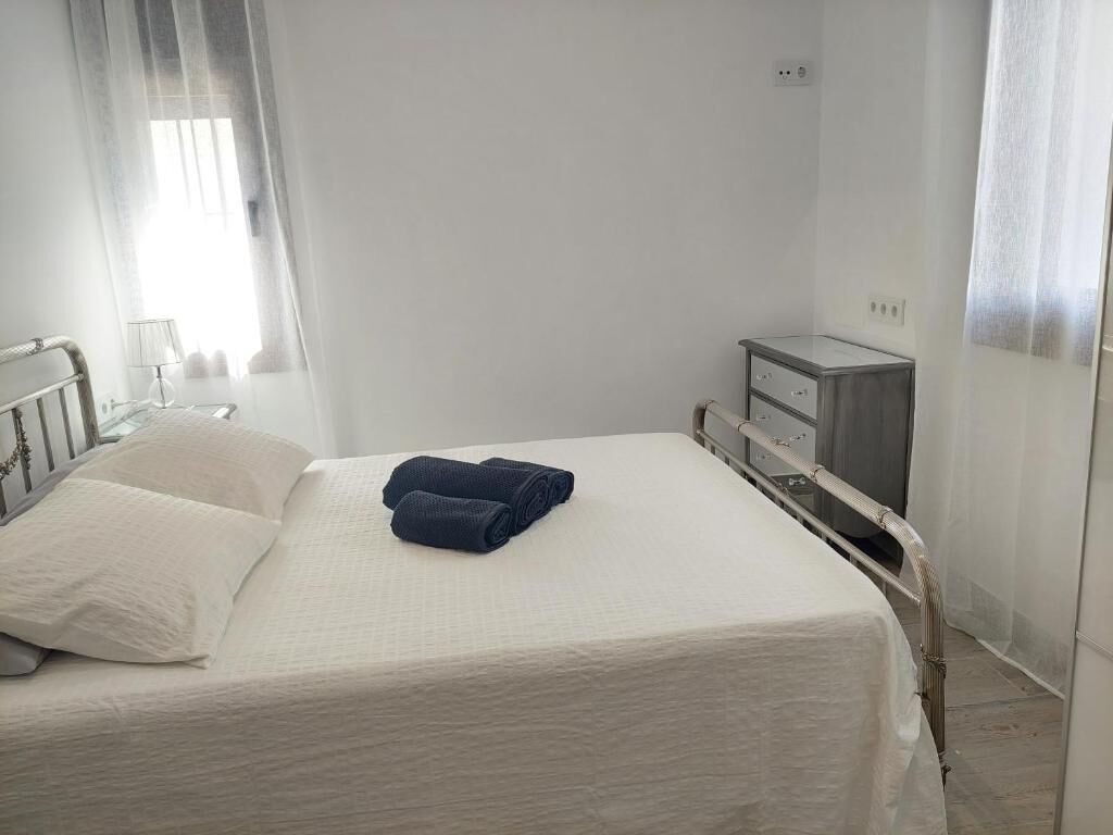 Un lit simple avec un matelas blanc et une serviette bleue, une table de chevet avec une lampe et une petite commode avec des tiroirs.