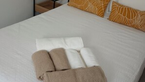 A neatly made bed with white and brown linens, a small bedside table with a lamp, and a plain wall. - El Rincon de San Fermin (Zizur Mayor)