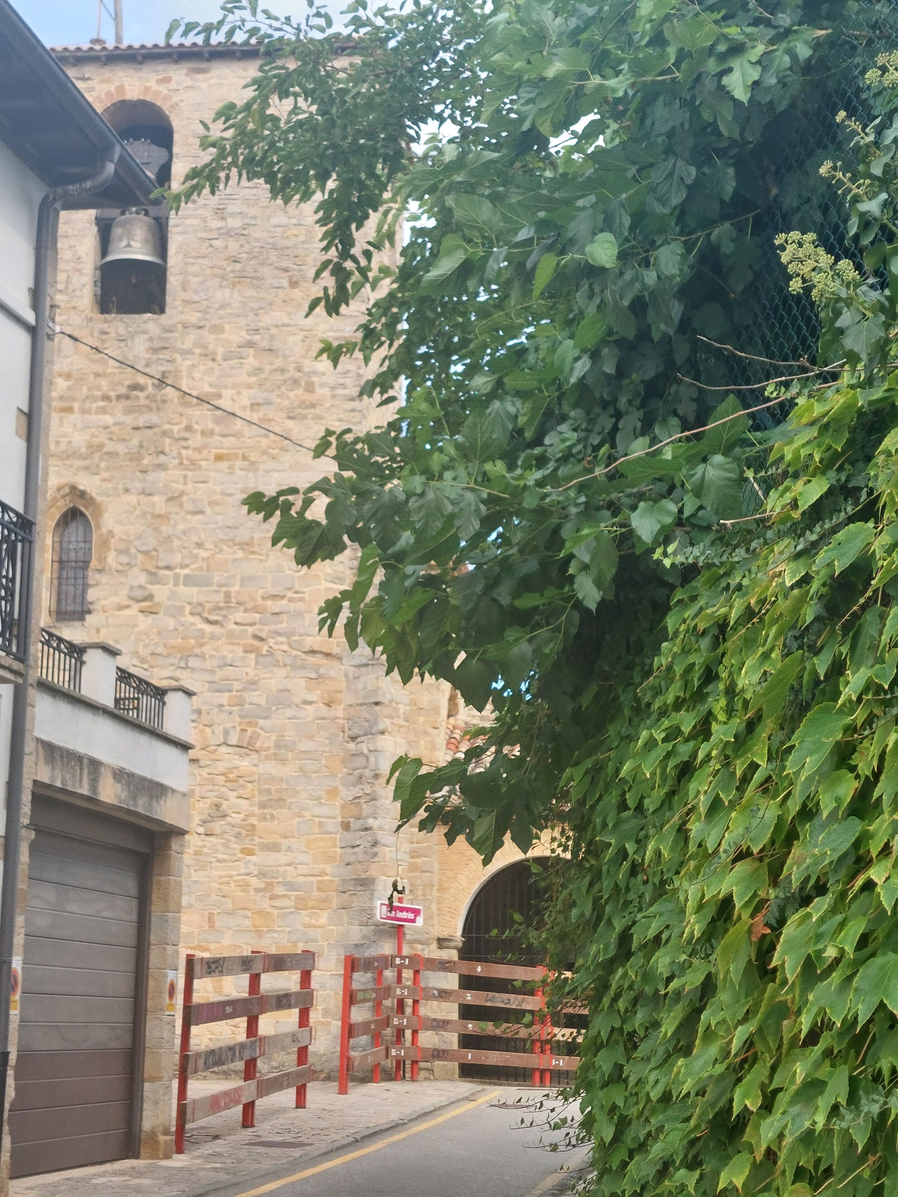 Un edificio de piedra con una torre de campanas, una entrada porticada y un árbol en primer plano.