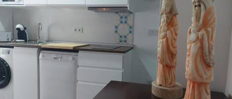 A modern kitchen with white cabinets, a microwave, a dishwasher, and a sink. There are two statues on a dark countertop.