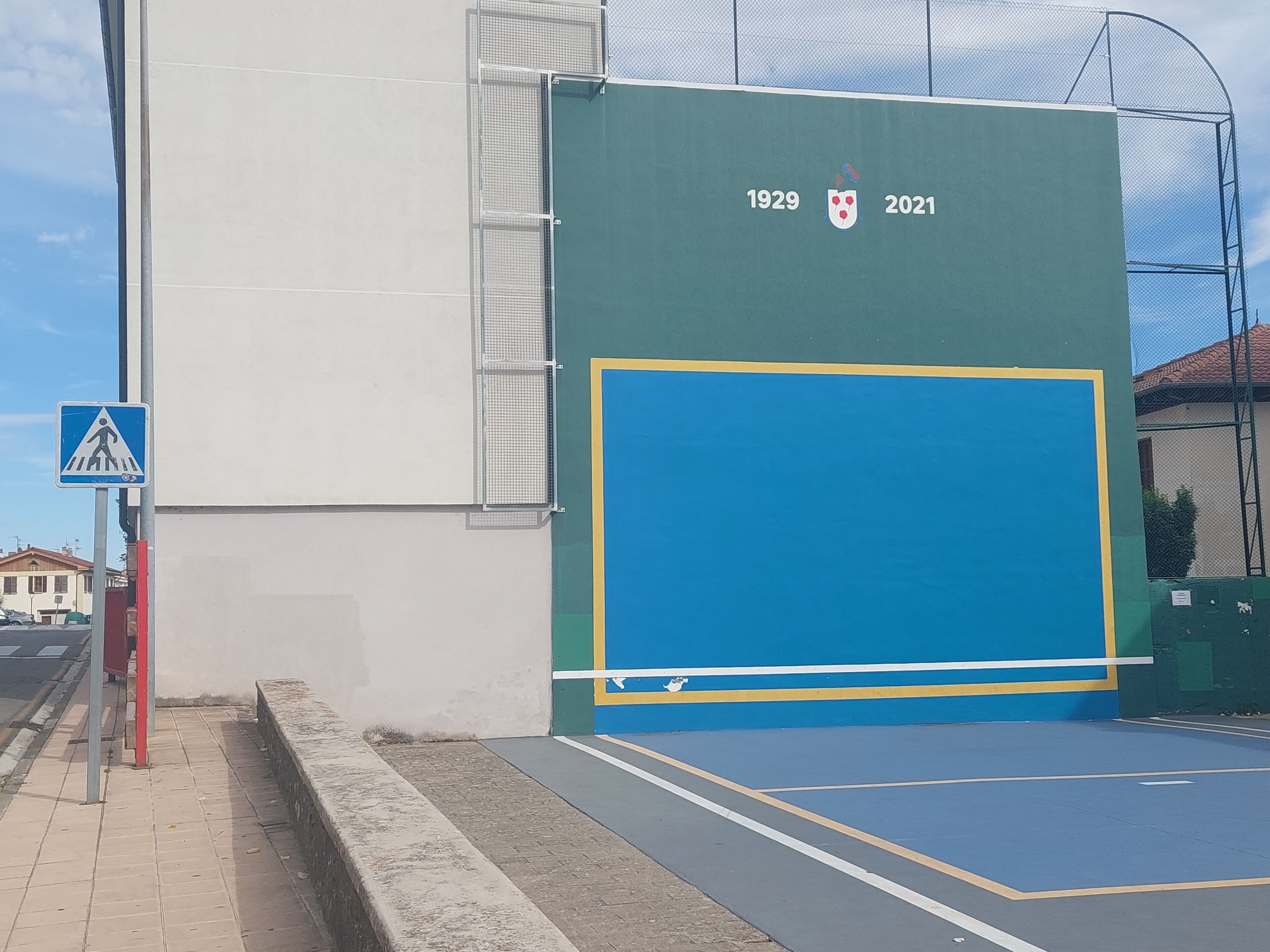 Un edificio con una puerta azul grande, una señal de paso de peatones y la inscripción del año '1929-2021'.