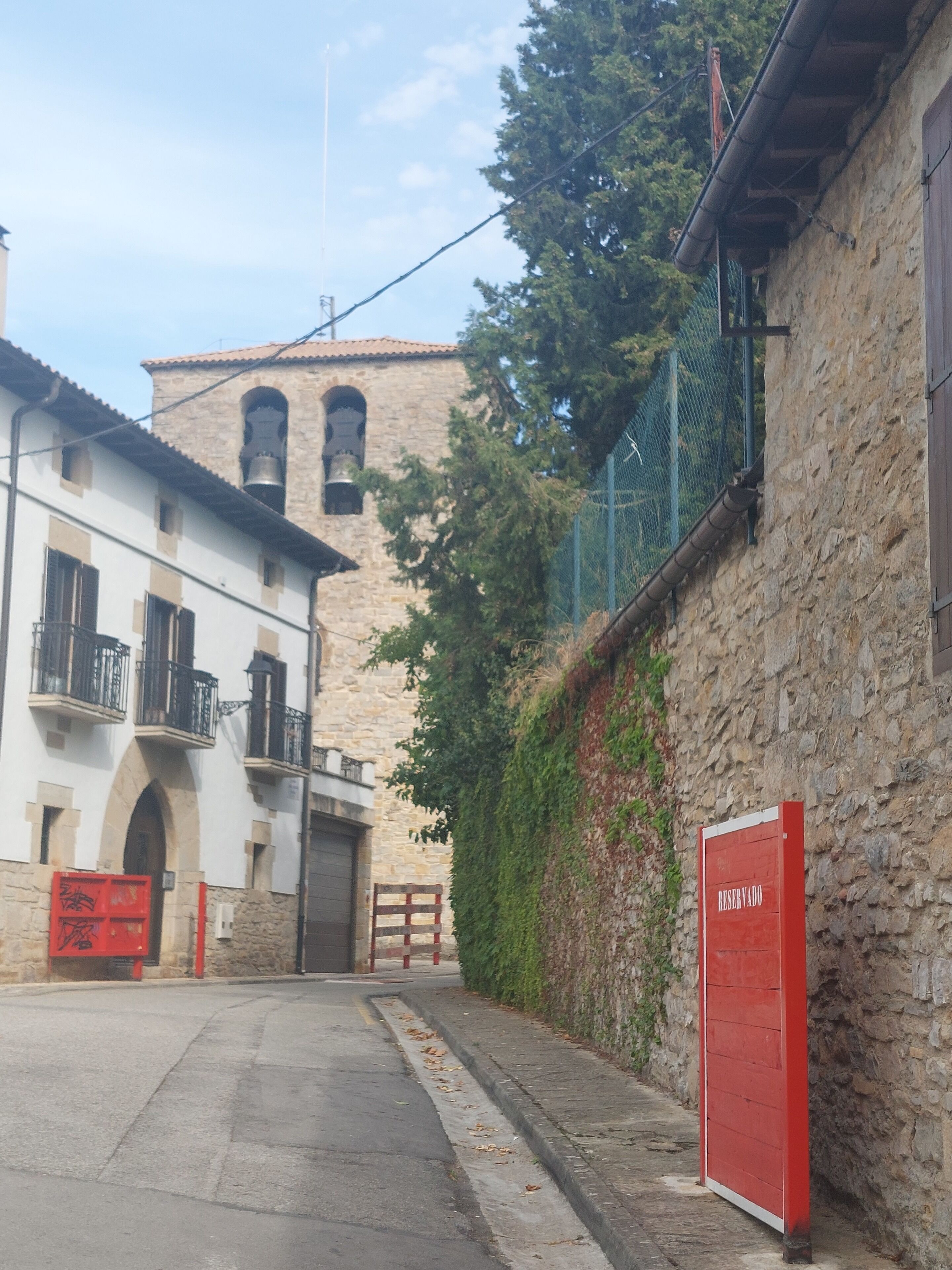 A narrow street with a stone building, a bell tower, and a red sign indicating a reserved area.