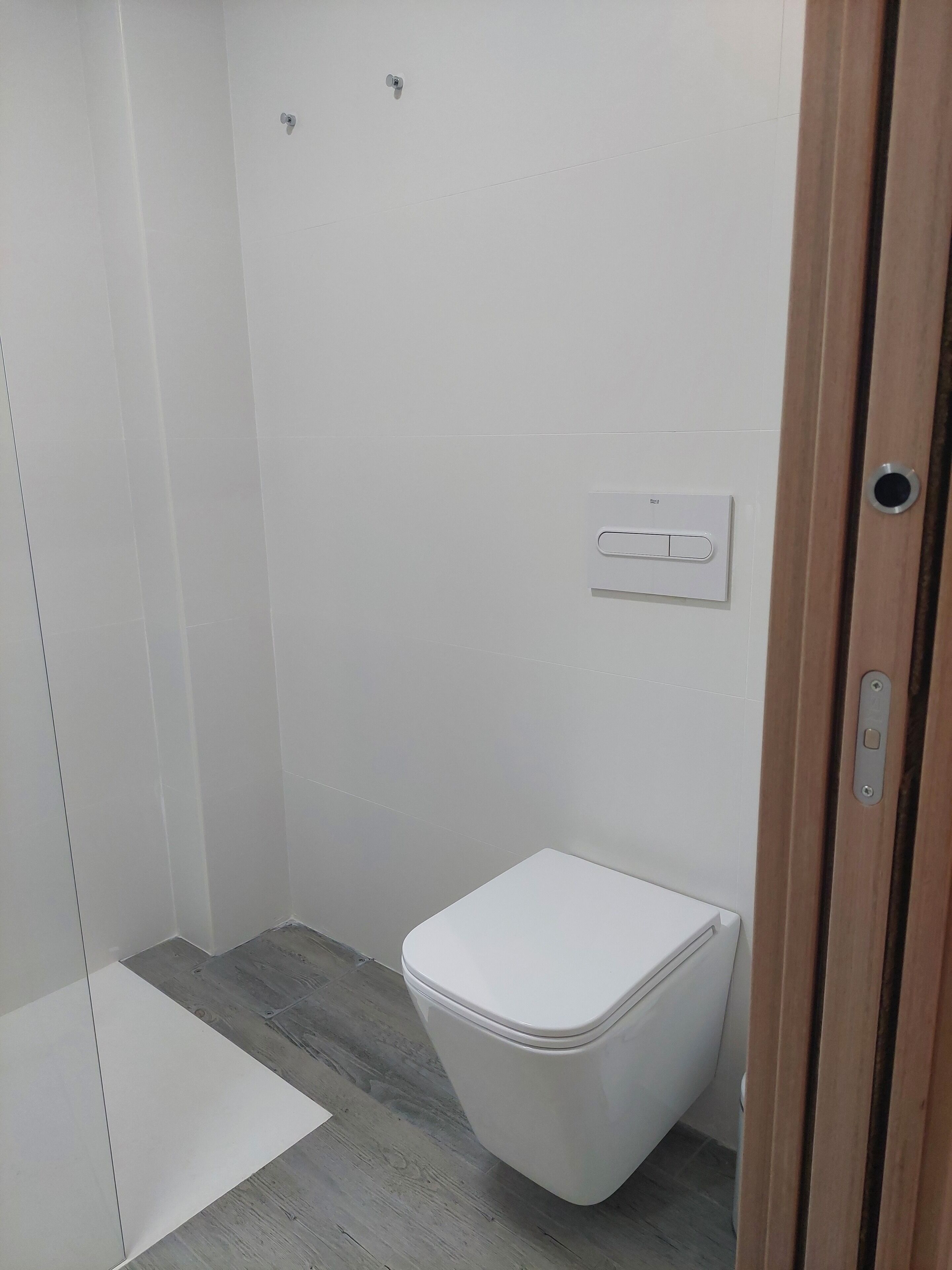 A bathroom with a white toilet, a shower, and a light switch on the wall.