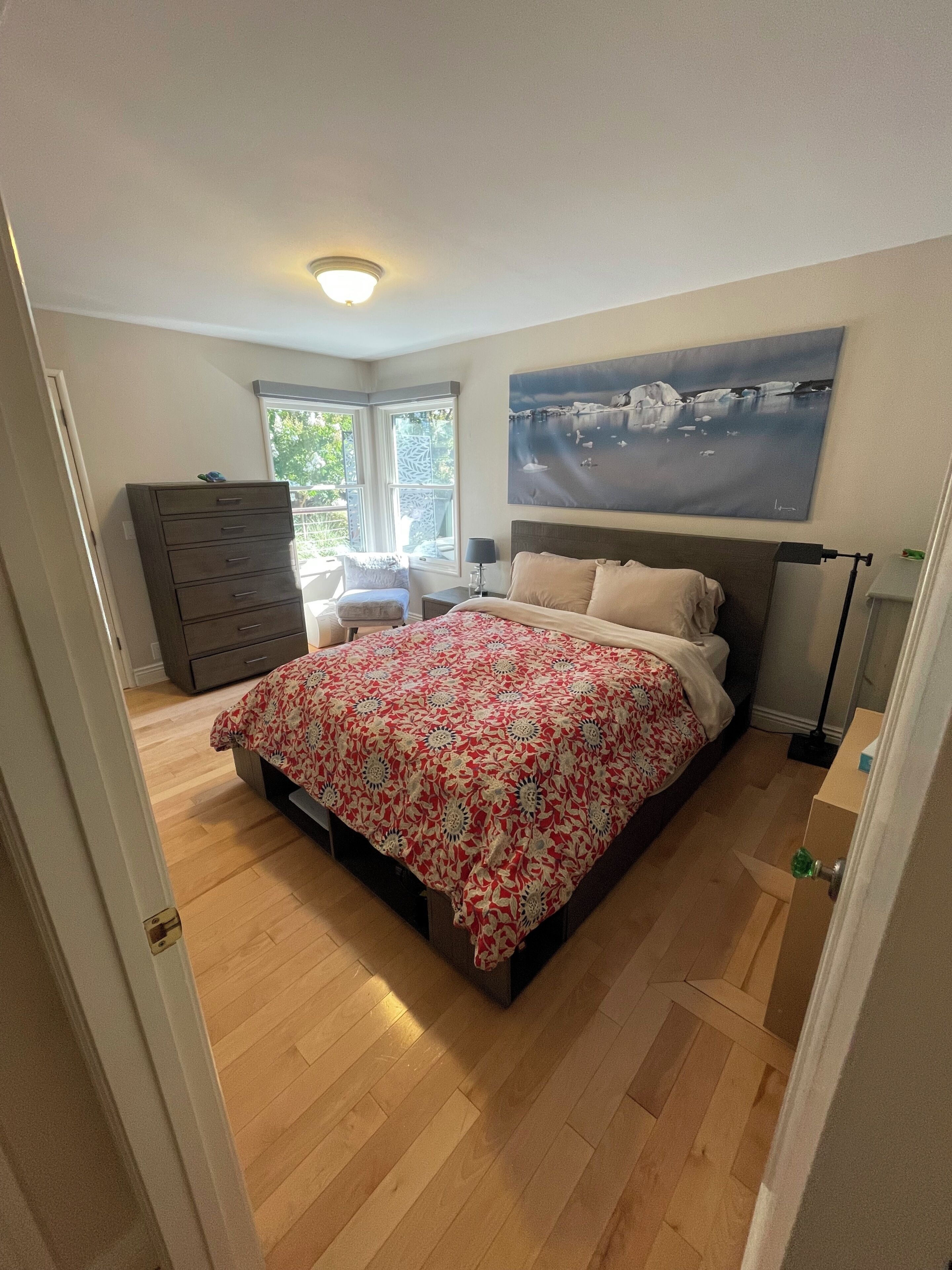 Un dormitorio con cama, cómoda, silla y una obra de arte en la pared.
