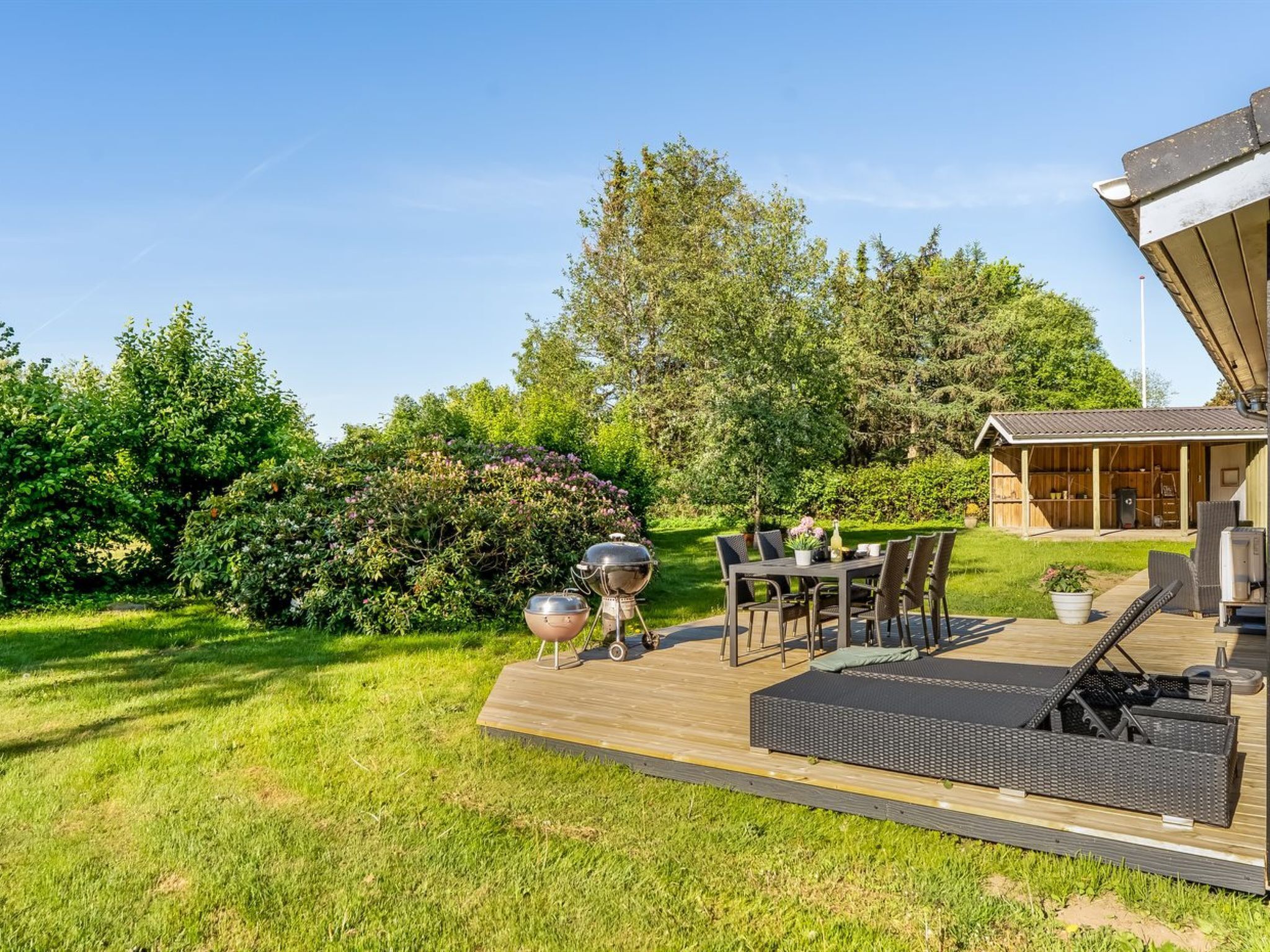 Terraza de madera con mobiliario exterior, una parrilla y un área cubierta con espacio de almacenamiento.