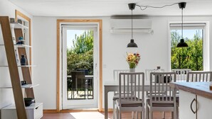 Een moderne keuken met witte kasten, een houten ladder, een eethoek met witte stoelen en een uitzicht door de deur op een terras.
