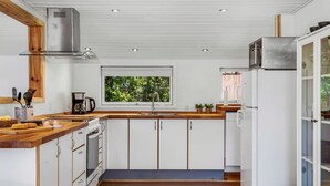 Een moderne keuken met witte kasten, houten aanrechtbladen, een roestvrijstalen afzuigkap en een raam met uitzicht op groen.
