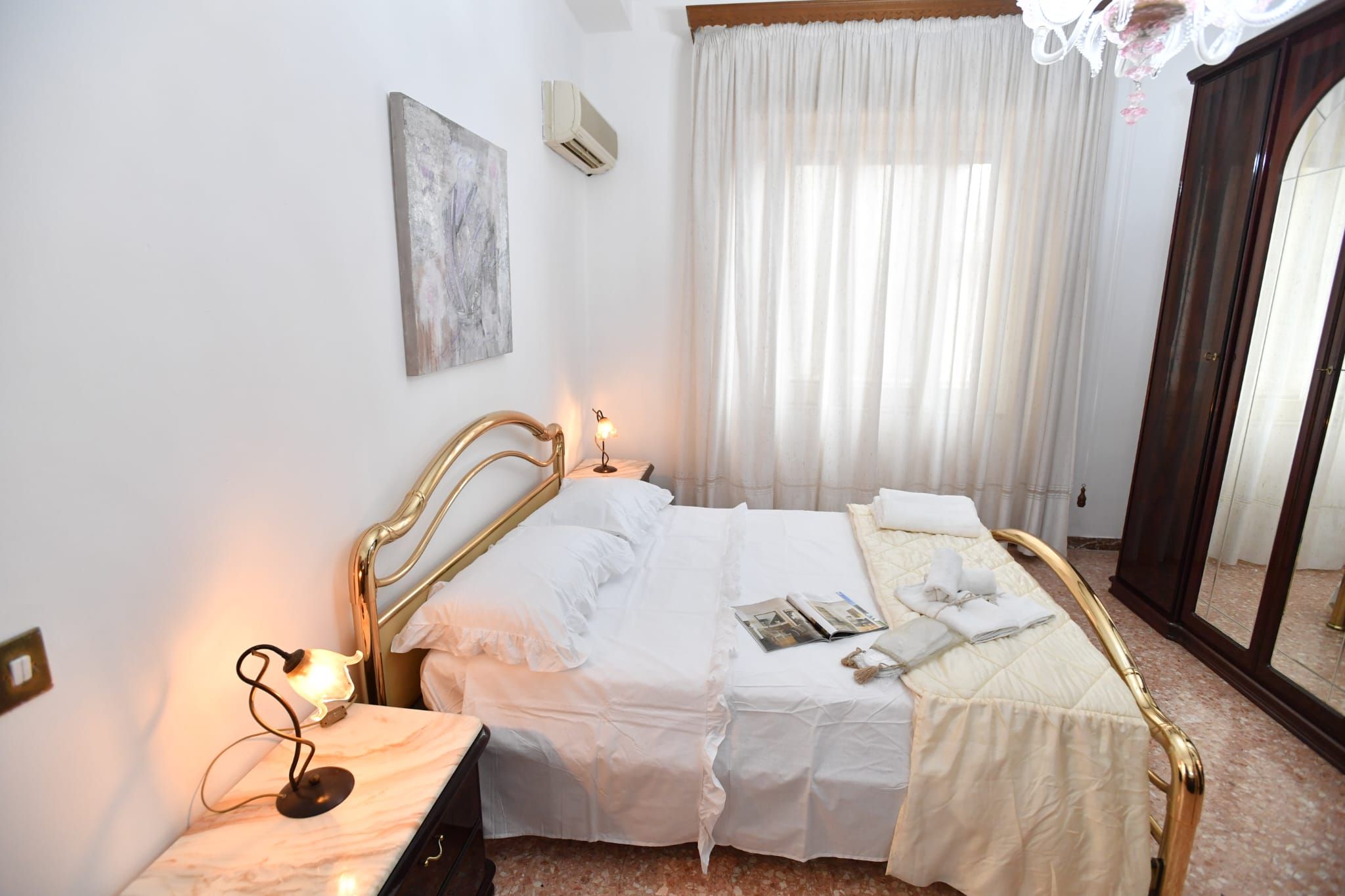 Un letto rifatto con lenzuola bianche, una lampada da comodino e un tavolino con lampada.