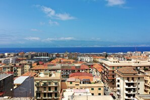 Paesaggio costiero con edifici urbani densi, cielo azzurro limpido e vista sul mare.