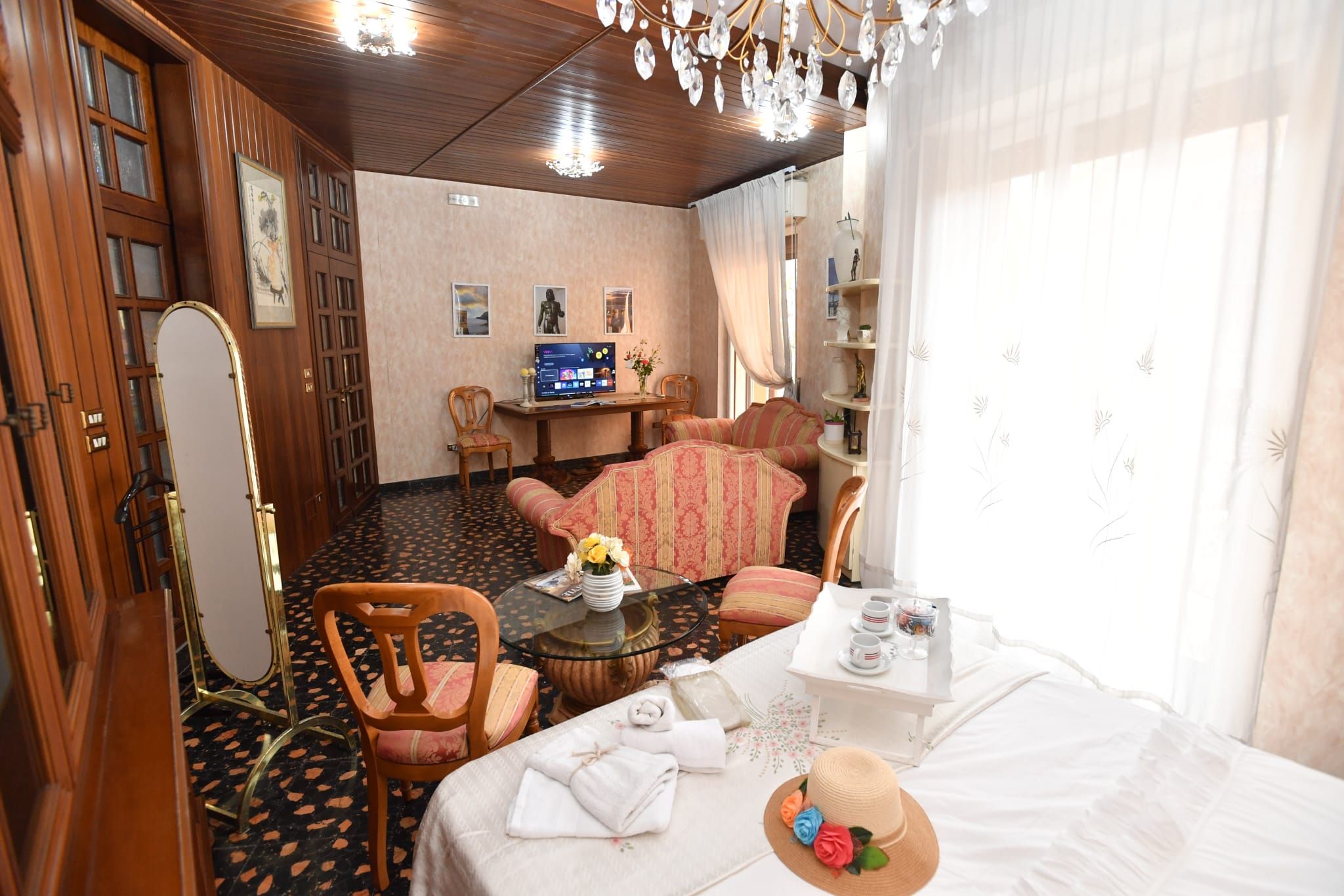Una camera d'albergo con un letto, una zona salotto con divano e poltrone, una televisione e una scrivania con un computer.