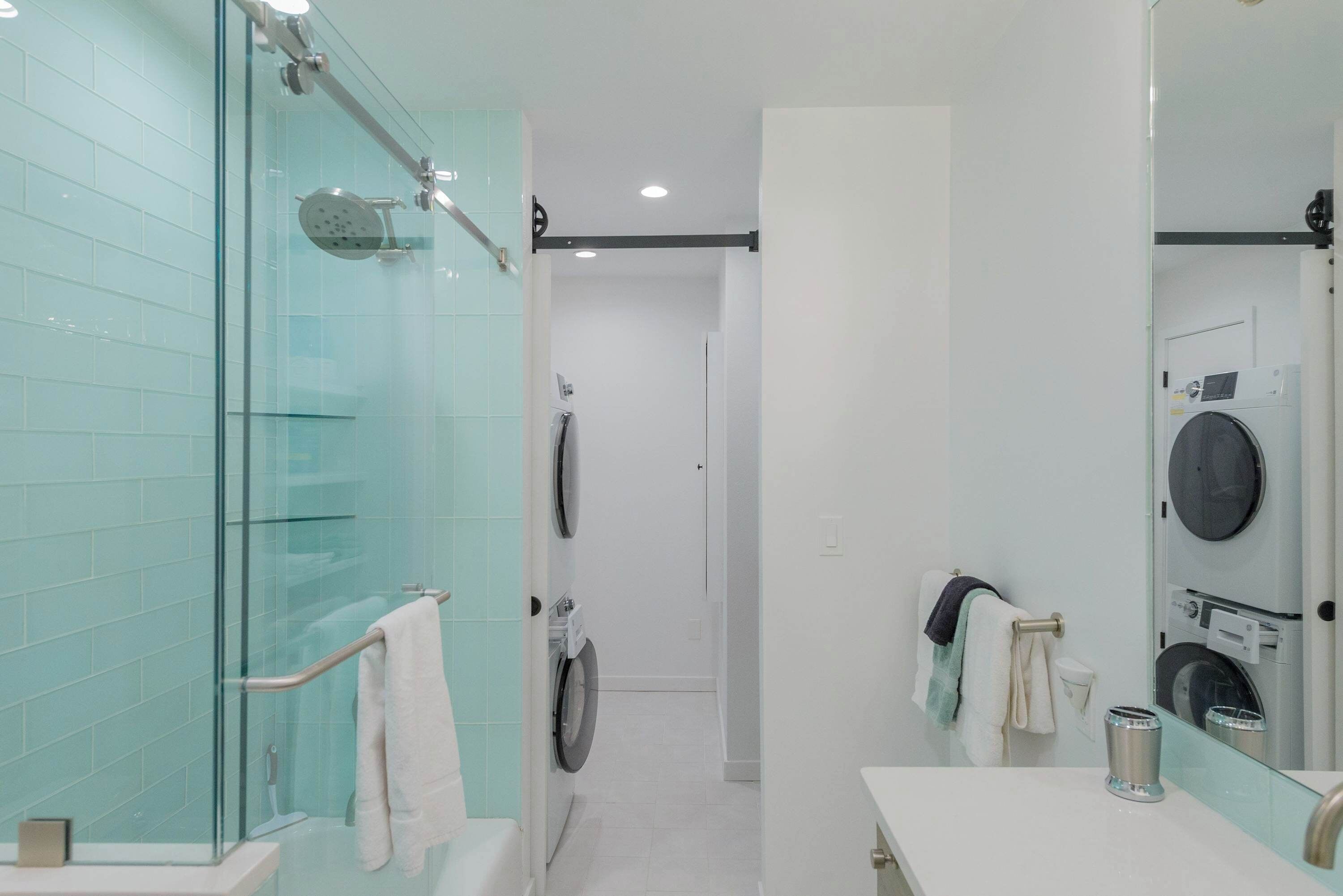 Une salle de bain moderne dotée d’une douche à parois de verre, d’un lave-linge encastré et d’un grand miroir.