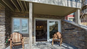 Une façade en pierre avec un porche abrité, deux fauteuils Adirondack en bois et une porte vitrée donnant sur l’intérieur.