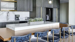 Une cuisine moderne avec des meubles gris, un îlot central agrémenté de plantes, un réfrigérateur encastré et un coin repas avec des chaises en marbre.