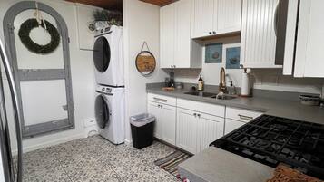 Une cuisine dotée d’un îlot central, de meubles blancs, d’un lave-linge, d’une poubelle et d’une couronne décorative.