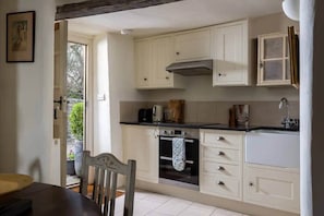 Una cocina con armarios blancos, estufa, pileta y ventana.