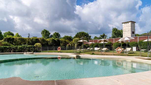 A swimming pool with a tiled deck, lounge chairs, umbrellas, and a lifebuoy. - Tenuta Primero Grado Family Collection (Grado)