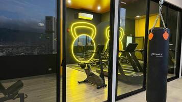 Une salle de sport équipée de matériel d’exercice, d’un sac de frappe et offrant une vue sur la ville grâce à de grandes fenêtres.