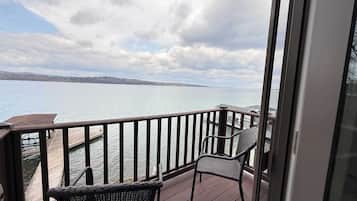 A balcony with a view of a lake, a wooden deck, and two wicker chairs.