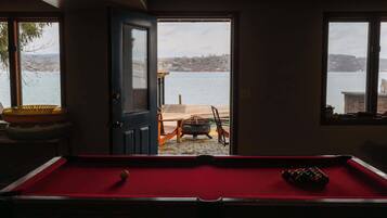 A pool table with a red felt surface, a door leading outside, and a view of a lake and distant buildings.
