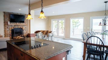 Una cocina con una isla central, una chimenea de piedra, un televisor de pantalla plana y un comedor con sillas y una mesa.